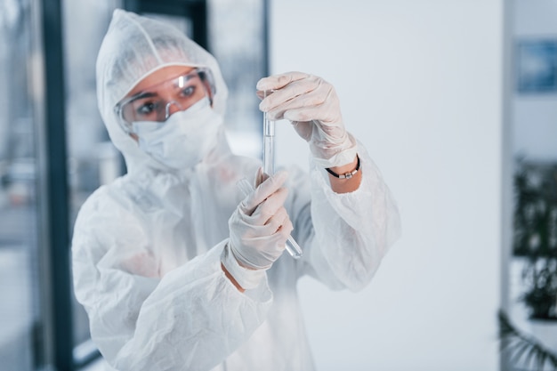 Contém tubos de ensaio. Retrato de cientista médico feminino no jaleco, óculos de defesa e máscara