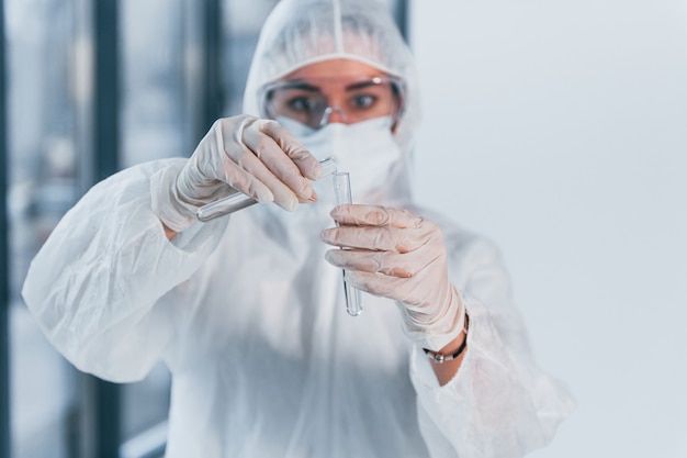 Contém tubos de ensaio. Retrato de cientista médico feminino no jaleco, óculos de defesa e máscara