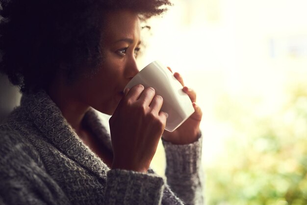 Contemplaciones de café Toma de una joven relajada disfrutando de una taza de café mientras está sentada junto a una ventana en casa