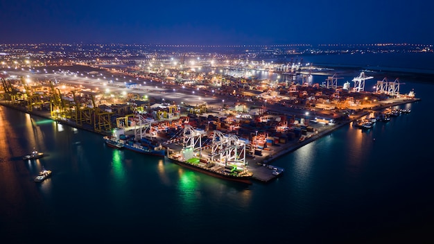 Contenedores de almacenamiento de la terminal del puerto y contenedores de carga de carga y descarga en la noche vista aérea