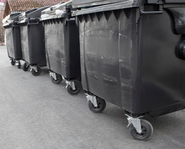 Los contenedores de basura de plástico negro llenos de basura esperando la recolección en una calle suburbana