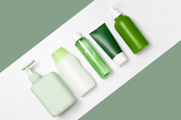 Contenedores de diferentes tamaños y formas para tónico limpiador, tónico, jabón y champú sobre fondo blanco y verde. Productos de belleza orgánicos naturales.