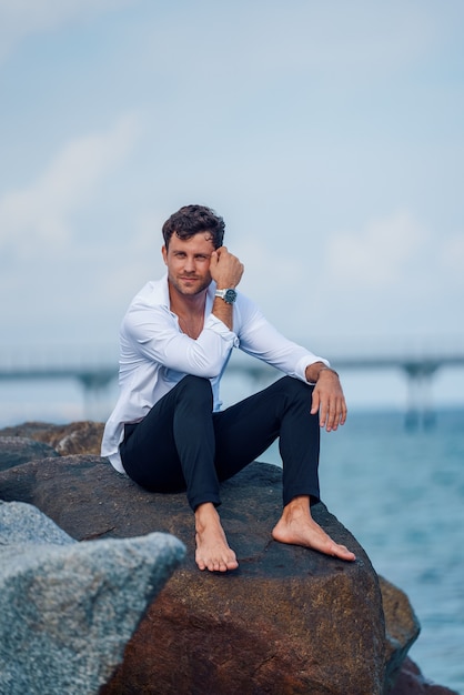 Contenido hombre elegante en roca cerca del mar