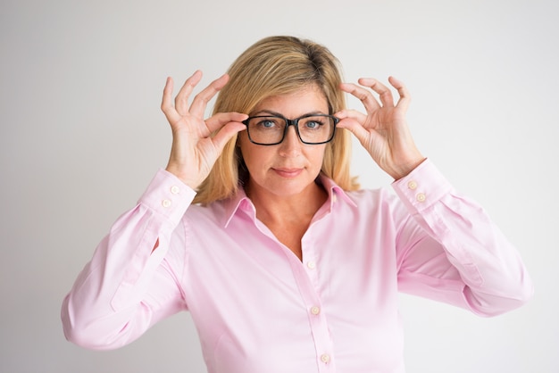 contenido de mediana edad atractiva mujer de pelo rubio mirando a la cámara y ajuste de gafas