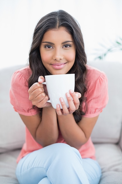 Contenido morena linda sentada en el sofá con taza