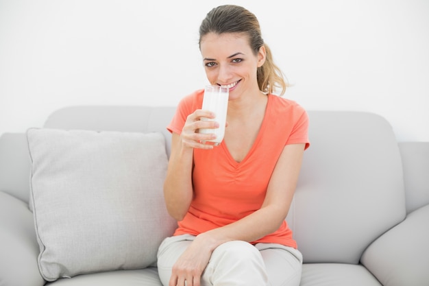 Contenido pacífica mujer sosteniendo un vaso de leche sonriendo alegremente a la cámara