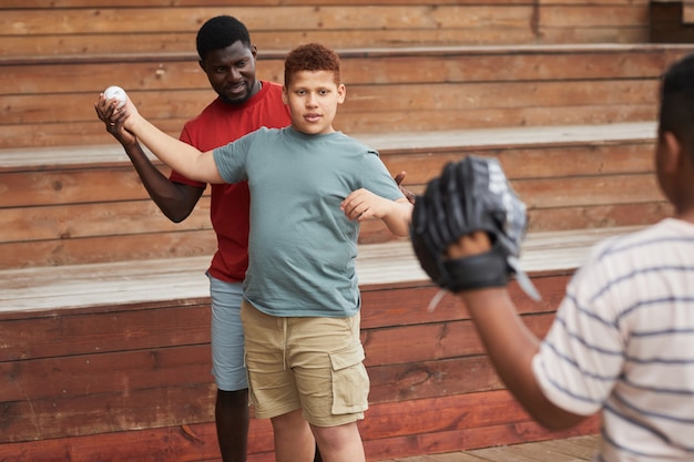 Foto contenido padre afroamericano ajustando el brazo del hijo mientras le enseña a lanzar