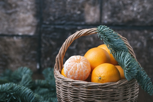 Foto contenido de vacaciones, mandarinas, mandarina pelada en una canasta de mimbre, vintage, rama de abeto, primer plano, fondo marrón oscuro, horizontal