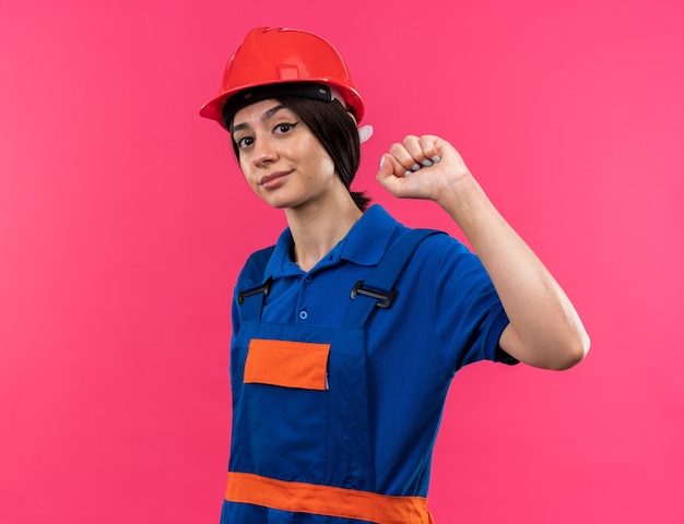 Contento mirando a la cámara joven constructor mujer en uniforme haciendo gesto fuerte