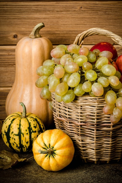 Conteúdo alimentar saudável, natureza morta de abóbora, mini abóboras, cesta de vime com uvas verdes e amarelas, maçãs vermelhas, em uma mesa escura, fundo de madeira