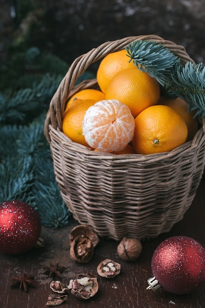 Conteúdo de férias, tangerinas, tangerina descascada em uma cesta de vime, vintage, ramo de abeto, bolas vermelhas de árvore de Natal, nogueira, fundo marrom escuro