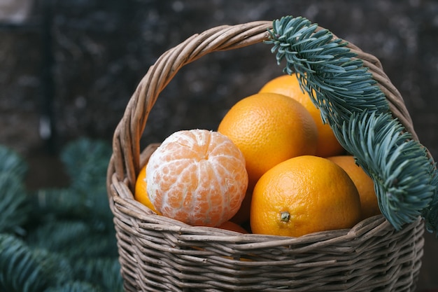 Conteúdo de férias, tangerinas, tangerina descascada em uma cesta de vime, vintage, ramo de abeto, closeup, fundo marrom escuro, horizontal