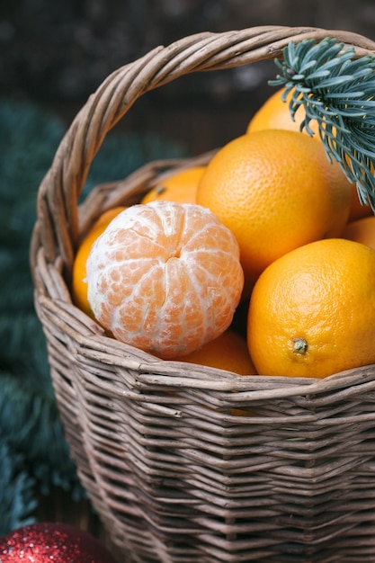 Conteúdo de férias, tangerinas, tangerina descascada em uma cesta de vime, vintage, ramo de abeto, closeup, fundo marrom escuro