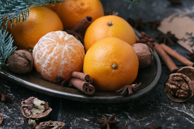 Conteúdo festivo, tangerinas, nozes, canela, cardamomo, prato de metal, galho de abeto, fundo marrom escuro, horizontal