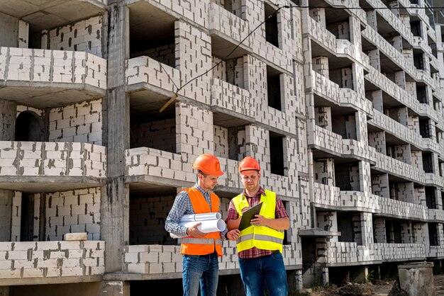 En el contexto del edificio en construcción, dos jóvenes trabajadores en overoles se paran de espaldas mirando el nuevo concepto de construcción de edificios