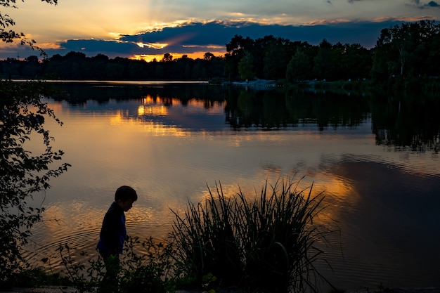 contorno de un niño al atardecer en el lago