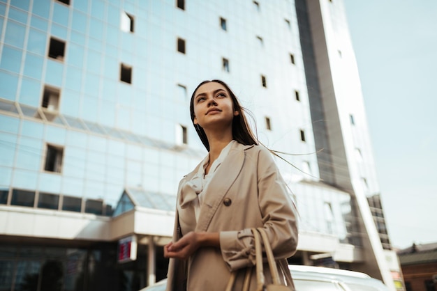 Contra el fondo de un edificio hecho de vidrio y hormigón, una chica mira soñadoramente a lo lejos