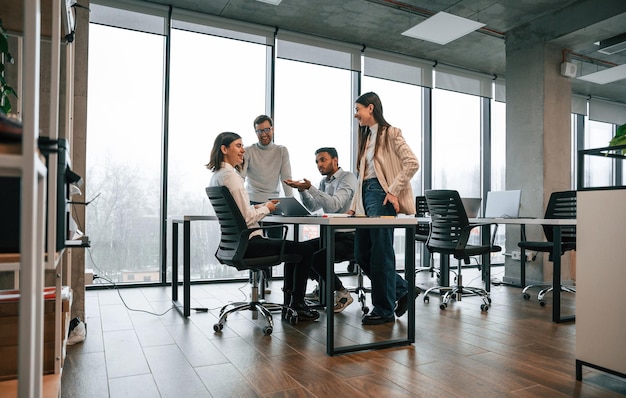 Contra grandes ventanas junto a la mesa Cuatro personas están trabajando en la oficina juntas