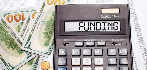 Contra o fundo de dinheiro e documentos está uma calculadora preta com o texto FINANCIAMENTO no placar. Conceito de negócios