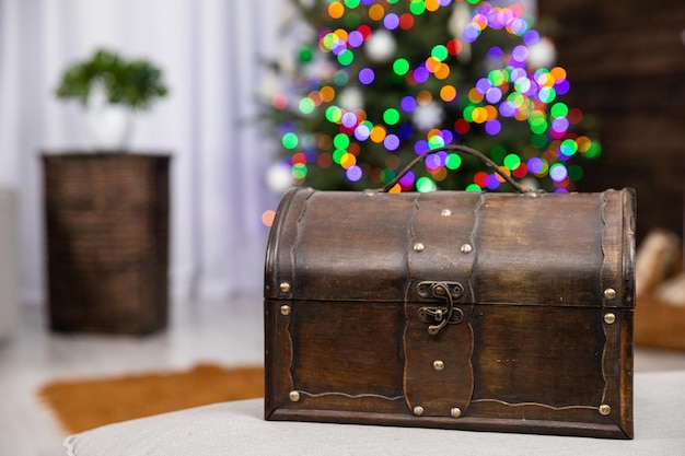 Contra o fundo difuso de uma árvore de Natal com luzes de Natal fica uma velha caixa de madeira