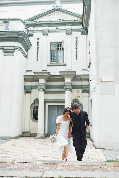 Contra o grande edifício da igreja Linda noiva com seu noivo está celebrando o casamento ao ar livre