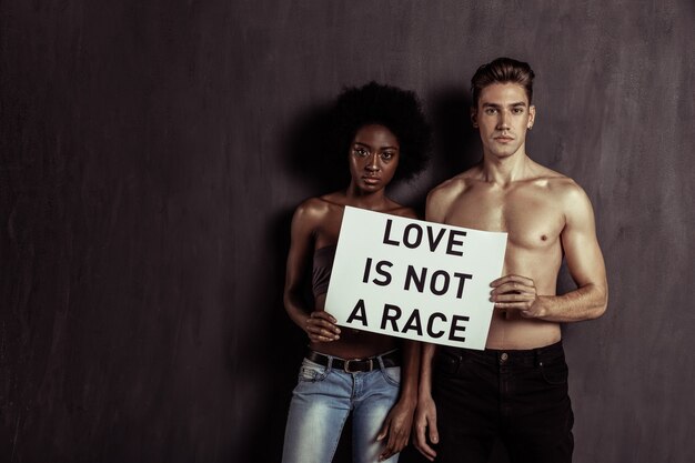 Contra los prejuicios. Grave pareja joven mirándote mientras está de pie junto con un cartel