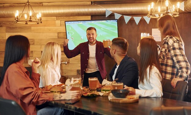 Contra tv grupo de jovens amigos sentados juntos no bar com cerveja