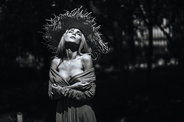 Contrastando retrato en blanco y negro de una chica sexy glamorosa con sombrero y vestido en la naturaleza