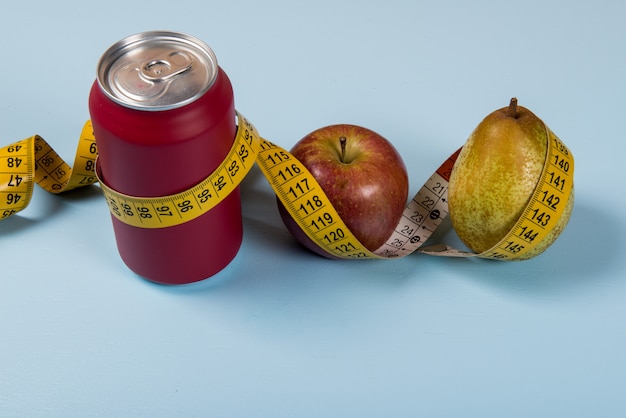 Contraste de vida saludable con lata de refresco y fruta con una cinta métrica