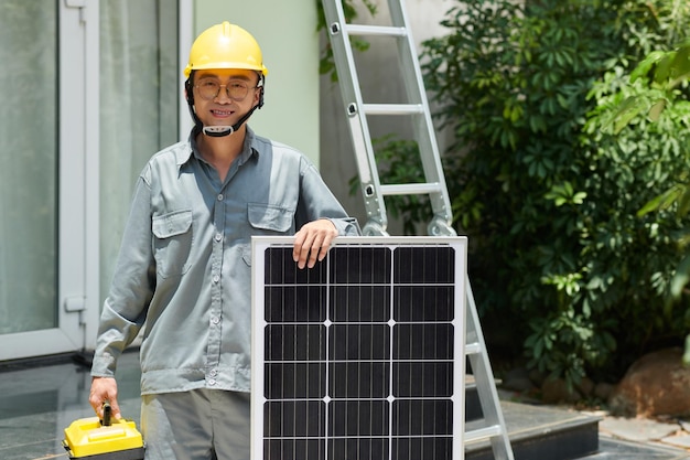 Contratista alegre en uniforme gris de pie junto al panel solar