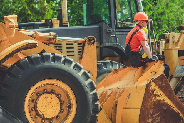 Un contratista caucásico descansando en el cubo de su excavadora