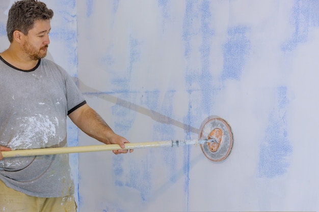 Foto contratista con llana de arena lijar el panel de yeso en la pared