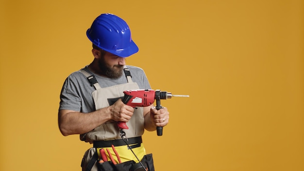 Contratista reparador perforando clavos con taladro eléctrico, trabajando  con máquina de pistola de tornillo en el edificio de construcción. usar  pistola de clavos y usar casco con overoles para hacer renovaciones.