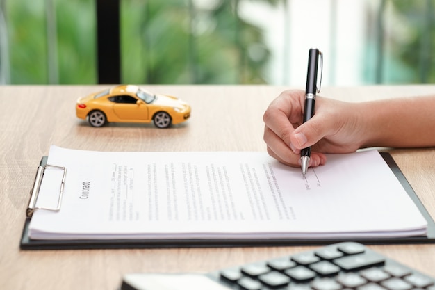 Contrato de assinatura do acordo de empréstimo do carro da mulher com brinquedo e calculadora do carro na mesa de madeira.