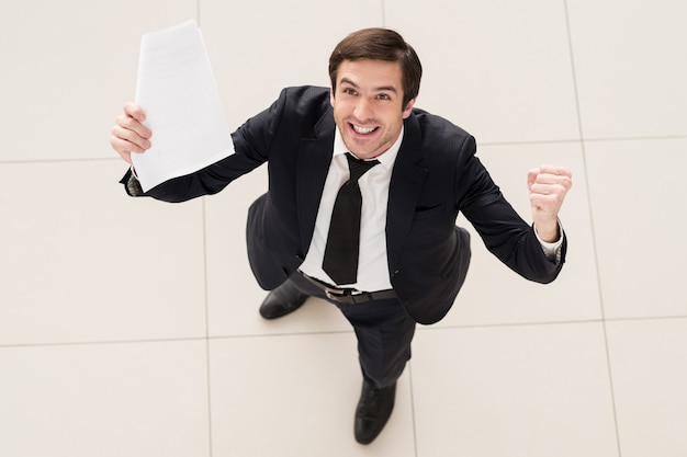 ¡Este contrato es mío! Vista superior del joven emocionado en ropa formal sosteniendo un papel en una mano y gesticulando