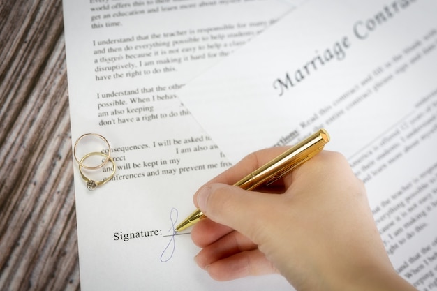 Contrato de matrimonio con dos anillos de bodas de oro y bolígrafo de oro, acuerdo prenupcial, cierre macro, firmar con signanture, documento, concepto de acuerdo romance