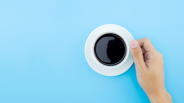 Un control masculino de la mano una taza de café en el fondo azul, visión superior.