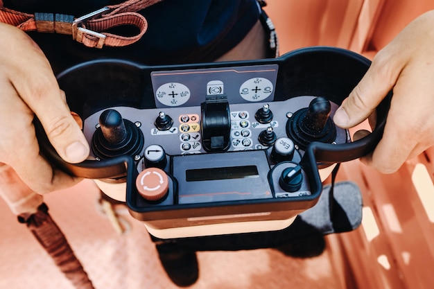 Control remoto de un coche grúa elevador en manos de una persona. Un panel con joysticks y botones para controlar el cucharón telescópico de la grúa.