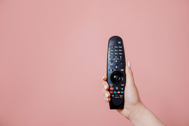 Control remoto de TV en mano femenina en pared rosa