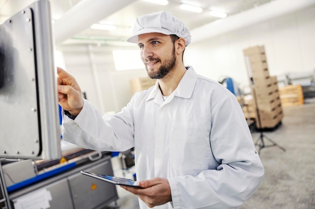 Un controlador de calidad de la fábrica de carne que trabaja con tabletas y máquinas de carne en la fábrica