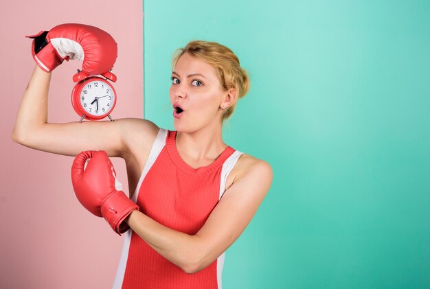 Controlar el tiempo Boxeador peleando con reloj despertador Tiempo para entrenamiento de boxeo Puntualidad y eficiencia personal Habilidades de gestión del tiempo Batalla por la autodisciplina Mujer sosteniendo guantes de boxeo de reloj