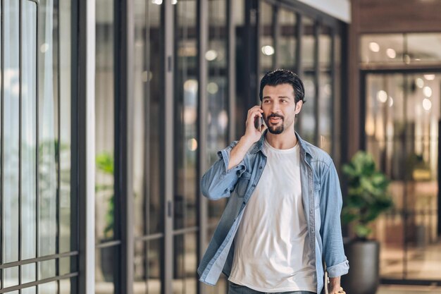 Conversación del trabajador en el teléfono inteligente y caminando dentro del edificio