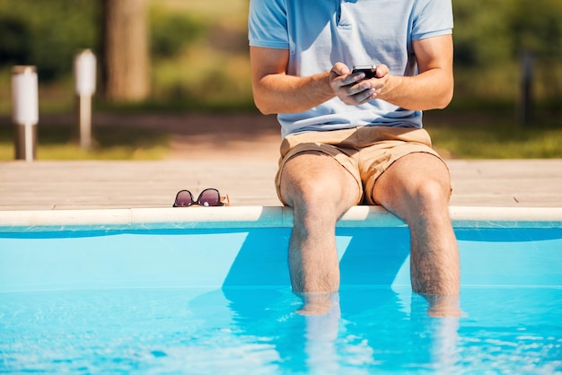 Conversando com amigos. imagem recortada de um homem sentado à beira da piscina digitando algo no celular