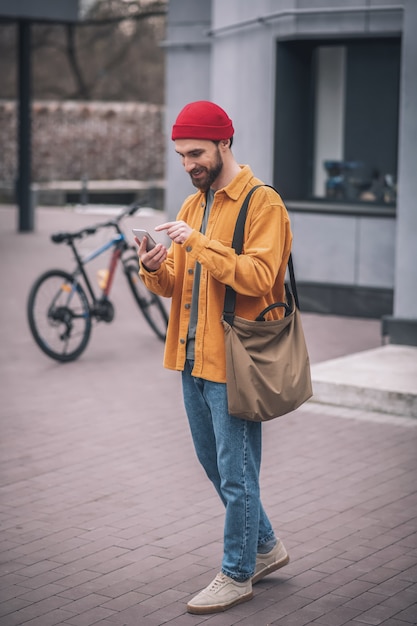 Conversando. Homem com chapéu vermelho e jaqueta laranja com seu smartphone nas mãos