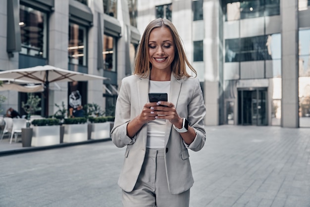 Foto converse com o cliente. mulher jovem e bonita de terno usando telefone inteligente e sorrindo