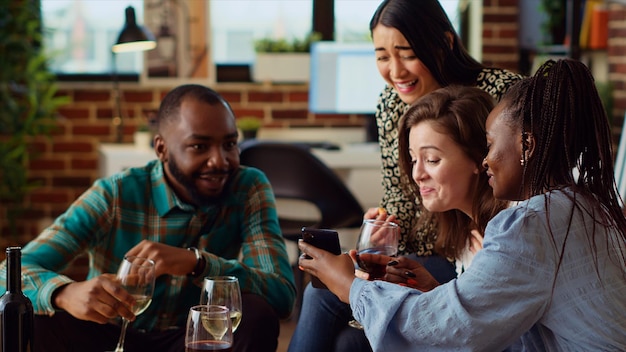 Convidados alegres na sala de estar vendo clipes da internet no telefone móvel enquanto bebem vinho