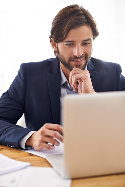 Convirtiendo el papeleo en ganancias. Un apuesto hombre de negocios que trabaja en su computadora portátil en su escritorio.