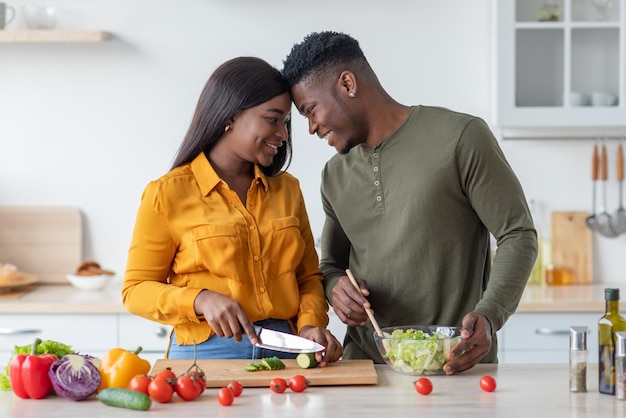 Cónyuges afroamericanos felices que se unen en la cocina mientras preparan juntos un almuerzo saludable