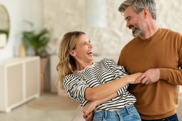 Cónyuges alegres de mediana edad bailando en la sala de estar en casa