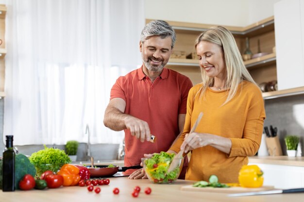 Cónyuges amorosos alegres haciendo ensalada de verduras saludables juntos